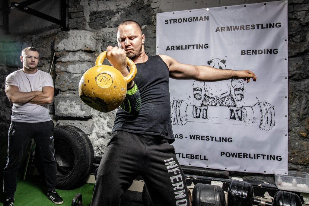 A strongman engages in kettlebell lifting, showcasing power and strength indoors.